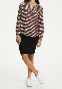 Blusa a maniche lunghe rossa e bianca a fantasia con scollatura a V, abbinata a una gonna nera fino al ginocchio e sneakers bianche. Tessuto morbido, vestibilità comoda.