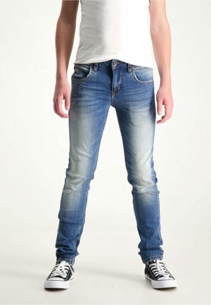 Niebieskie dżinsy o dopasowanym kroju z efektem sprania na udach, pięcioma kieszeniami oraz metalowym zapięciem na guzik. Połączone z czarnymi trampek z płótna.