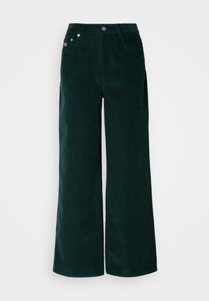 Videbenne corduroy bukser i mørkegrønn, med en teksturert overflate, frontlommer og metallknapplukking. Ingen synlige dekorasjoner.