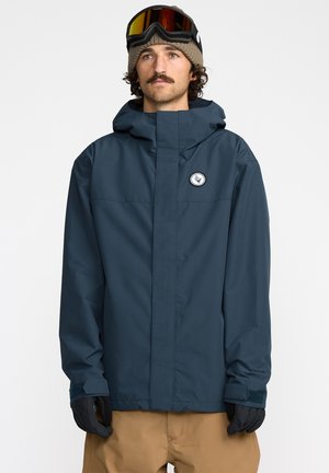Veste imperméable bleu foncé avec une fermeture éclair avant, capuche ajustable et patch logo. Équipée de poignets élastiques et d'une texture de tissu lisse et résistante.