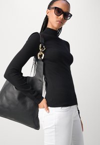 Black long-sleeve top with a high neck, paired with a large black leather tote bag featuring a gold hardware accent, and white pants.