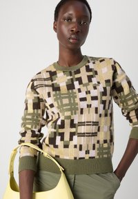 Pull en tricot multicolore avec un motif géométrique dans des teintes de jaune, vert, marron et lilas ; encolure ronde et poignets côtelés.