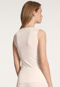 Mouwloos, lichtroze tanktop gemaakt van zachte stof. Heeft een eenvoudig, glad ontwerp met een ronde halslijn en een rechte, aangesloten silhouette.