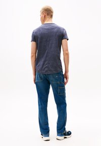 T-shirt texturé bleu marine à manches courtes, associé à un pantalon cargo en denim bleu avec poches latérales et coupe décontractée. Chaussures blanches et bleu marine.