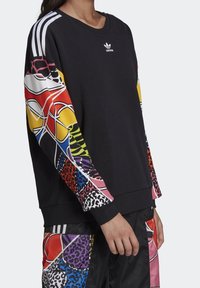 Zwarte sweatshirt met kleurrijke patroonsleeves, voorzien van dierenprints en gedurfde geometrische ontwerpen. Adidas-logo op de borst, stijl met ronde hals.