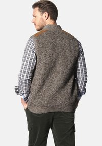 Brauner gestrickter Weste mit texturiertem Finish und beigen Schulterpatches, getragen über einem blau-weißen karierten Hemd. Rückansicht.