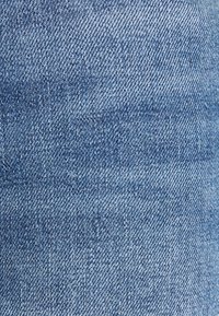 Tela de mezclilla en azul claro con un fino tejido en sarga, con variaciones sutiles en el sombreado y la textura, características típicas de la mezclilla.