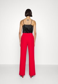 Czarna satynowa koszulka na cienkich ramiączkach w zestawie z wysokim stanem i szerokimi nogawkami czerwonych spodni. Gładka tkanina bez widocznych wzorów.