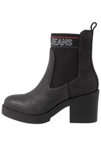 Mustat nilkkurit, joissa on teksturoitu synteettinen päällinen, joustavat sivupaneelit, logo-juova ylhäällä ja paksu pohja.