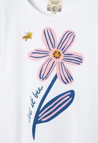 Chemise blanche avec fleur rose et bleue, petite abeille jaune, et texte manuscrit « let it bee » le long de la tige de la fleur.