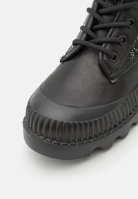 Bottines en cuir noir avec semelle en caoutchouc texturée, bout rond et fermeture à lacets, présentant des coutures décoratives et une finition lisse.