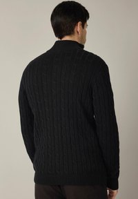 Czarny dzianinowy sweter z ażurowym wzorem, wysokim kołnierzem oraz ściągaczami na rękawach i u dołu. Widok od tyłu podkreśla teksturowany design.