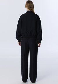 Zwarte oversized sweatshirt met hoge kraag en geribde mouwen, gecombineerd met bijpassende broeken met wijde pijpen en een op maat gemaakte pasvorm met subtiele naden.