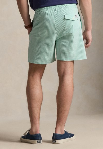 Πράσινα και άσπρα ριγέ σορτς με ελαστική μέση, τσέπη στο πίσω μέρος και άνετη εφαρμογή, σε συνδυασμό με μπλε παπούτσια τύπου slip-on.