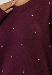 Burgundin paita, jossa on pyöreä pääntie, tekstuurin omaava neulos ja satunnaisia strassiaksentteja. Pehmeä materiaali ja ribbiresorit.