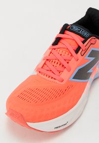 Bright coral running shoe with mesh upper, black accents, and light blue detailing. Features prominent lacing and textured surface for grip.