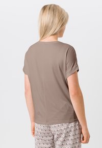 Bruine korte mouwen t-shirt met een zachte textuur en een eenvoudige, rechte snit. Heeft een naad aan de achterkant en wordt gecombineerd met een broek met een patroon in lichte kleuren.