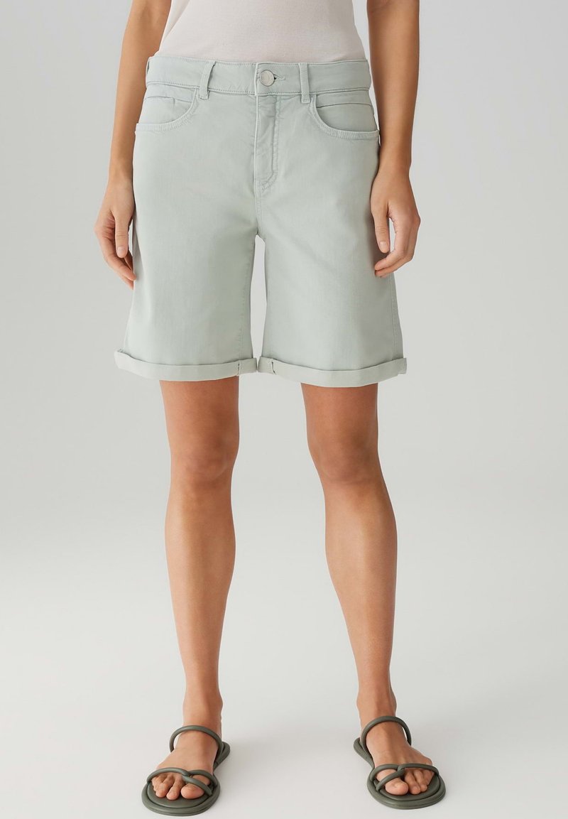 Shorts en denim vert clair avec un ourlet retroussé, design à cinq poches et fermeture à bouton à l'avant. Assortis à des sandales simples à semelle plate.