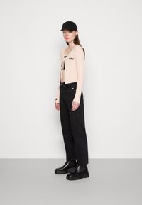 Heled roosa ribaga lühike kardigan, seotud esiosaga, must graafiline t-särk, kõrge vöökohaga mustad teksad ja mustad paksud slip-on saapad.