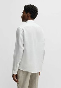 Witte lange mouwen linnen shirt met een bandkraag, met knoopmanchetten en een rechte zoom, gedragen over lichtgrijze broeken.