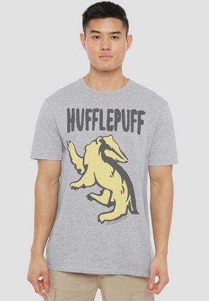 Young man wearing a gray t-shirt with a large yellow badger and "HUFFLEPUFF" text on the front, standing against a plain background.