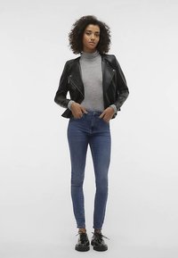 Melna ādas motociklistu jaka ar sudraba rāvējslēdzējiem, pelēks augsta apkakle džemperis, zilas šauras džinsa bikses un melni platformas apavi. Gluda tekstūra un pieguļošs dizains.