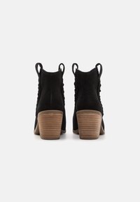 Botines de ante negro con una parte superior texturizada, que cuentan con un tacón de madera apilada y lengüetas en la parte trasera para facilitar su uso.