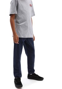 Graues T-Shirt mit kurzen Ärmeln und einem kleinen roten Logo, kombiniert mit marineblauen Jogginghosen und schwarzen Sneakers mit einer weißen Sohle und schwarzen Akzenten.