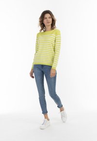 Maglione a righe giallo brillante e bianco, con maniche lunghe e collo rotondo. Indossato con jeans blu e sneakers bianche.
