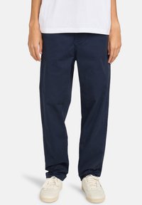 Navy blue, lightweight cotton pants with a relaxed fit. Features side pockets and cuffed hems, worn with white sneakers.
