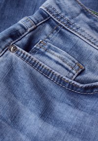 Jeans i denim har en ljusblå färg med en slät yta, synlig sömnad i en kontrasterande gul färg och en liten bakfickdetalj.