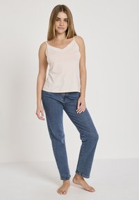 Lichtroze camisole met kantafwerking, gedragen met blauwe denim jeans. De top heeft dunne bandjes en een losse pasvorm, de stof lijkt glad.