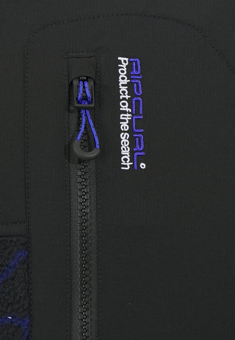 Material de traje de neopreno negro con una superficie texturizada. Presenta una cremallera central con un tirador azul. Incluye bordados en blanco y azul del nombre de la marca.