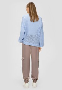 Jasnoniebieski, dzianinowy, oversize'owy sweter o luźnym kroju, w połączeniu z beżowymi spodniami cargo. Białe sneakersy dopełniają całokształt.