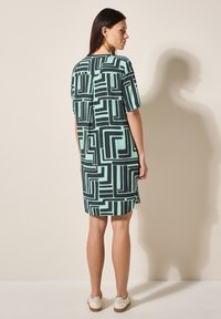 Kurzes Kleid in Mintgrün mit schwarzen geometrischen Mustern. Hat eine lockere Passform, knie-lange Säume und seitliche Schlitze für mehr Bewegungsfreiheit.