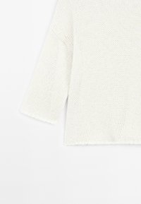 Jasna kremowa sweter wykonany na drutach, o luźnym kroju, z rękawami do łokcia i teksturowanym, otwartym splotem. Surowe krawędzie u dołu i rękawów.