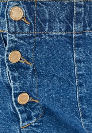 Denimstof in een rijke blauwe tint, met drie metalen knopen en contrasterend gele stiksels langs de naden en het zakgebied.