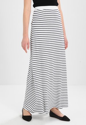 Femme portant une jupe maxi blanche avec de fines rayures horizontales noires et des chaussures plates pointues noires.
