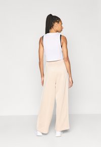 Bela kratka majica brez rokavov s črnimi naramnicami, kombinirana z bež hlačami širokih nogavic. Gladek material z elastičnim pasom, dolžina do tal.