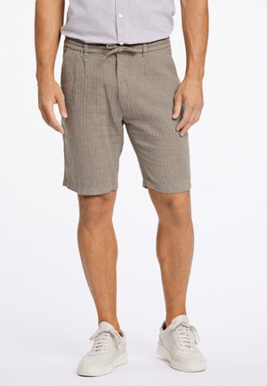 Shorts marron clair avec un design texturé à rayures et une taille élastique. Portés avec des baskets blanches, sans poches visibles.