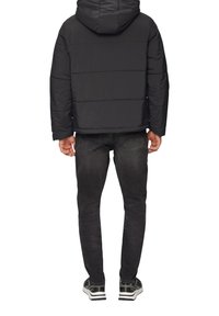 Schwarze Pufferjacke mit Kapuze, ausgestattet mit gestepptem Futter und einer cropped Passform, kombiniert mit dunklen Jeans und schwarzen Sneakers.