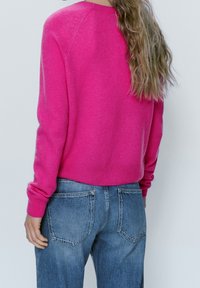 Pull en tricot rose vif à manches longues, avec des poignets et une taille côtelés, associé à un jean droit bleu délavé.