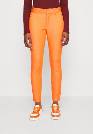 Lyse orange slim-fit bukser lavet af glat stof, med en frontlomme og ankellængde. Matchet med hvide og orange sneakers.