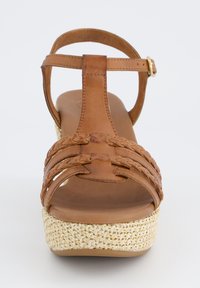 Hnědé kožené sandály s pletenými horními popruhy, T-řemínek a espadrilový styl tkané platformy. Ploché hnědé polstrované stélky.