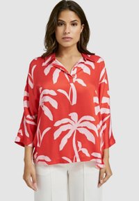 Rote Bluse mit kurzen Ärmeln, die einen weißen Palmblatt-Druck aufweist, mit einem kragenlosen Ausschnitt und einem lockeren Schnitt. Glattes, leichtes Material.