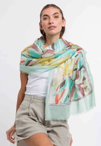 Sciarpa leggera e multicolore con motivi astratti in turchese, giallo e corallo. I bordi sono frangiati con un contrasto di colore.