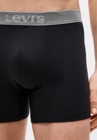 Homme portant un boxer noir avec une ceinture grise arborant le logo Levi's, visible de la taille jusqu'au milieu de la cuisse.