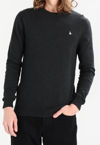 Ciemnoszary sweter z długim rękawem wykonany z fakturowanej tkaniny, z okrągłym dekoltem i małym, białym logo na lewej piersi.