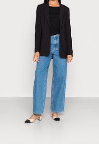 Sorte struktureret blazer, tætsiddende sort skjorte, højtaljede lyseblå vide bukser og beige blokhælede sko med sorte tåkapper.