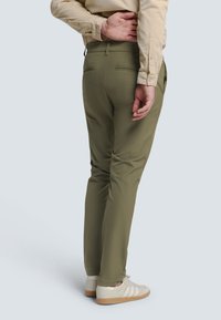 Olijf groene broek met een slim fit, met achterzakken en subtiele stiksels. Draag het met witte sneakers en een beige shirt.